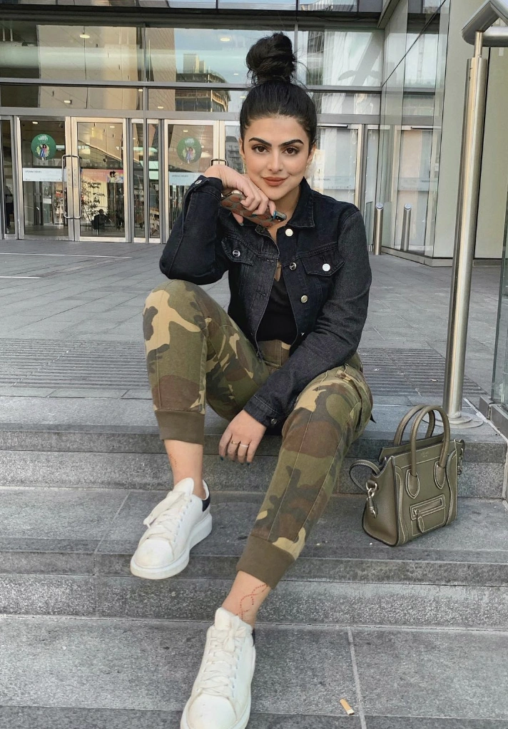 Camouflage Pants Outfit styled with a black denim jacket, black top, and white sneakers, accessorized with a mini handbag and a casual top bun hairstyle.