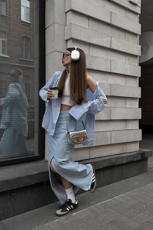 Trendy denim-on-denim look styled with black Adidas Samba Outfits, oversized blue shirt, crop top, and long denim skirt.