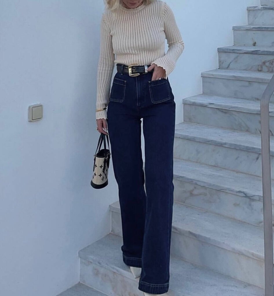 Chic wide leg pants outfit featuring dark denim with large front pockets, a ribbed beige sweater, and white pointed shoes.