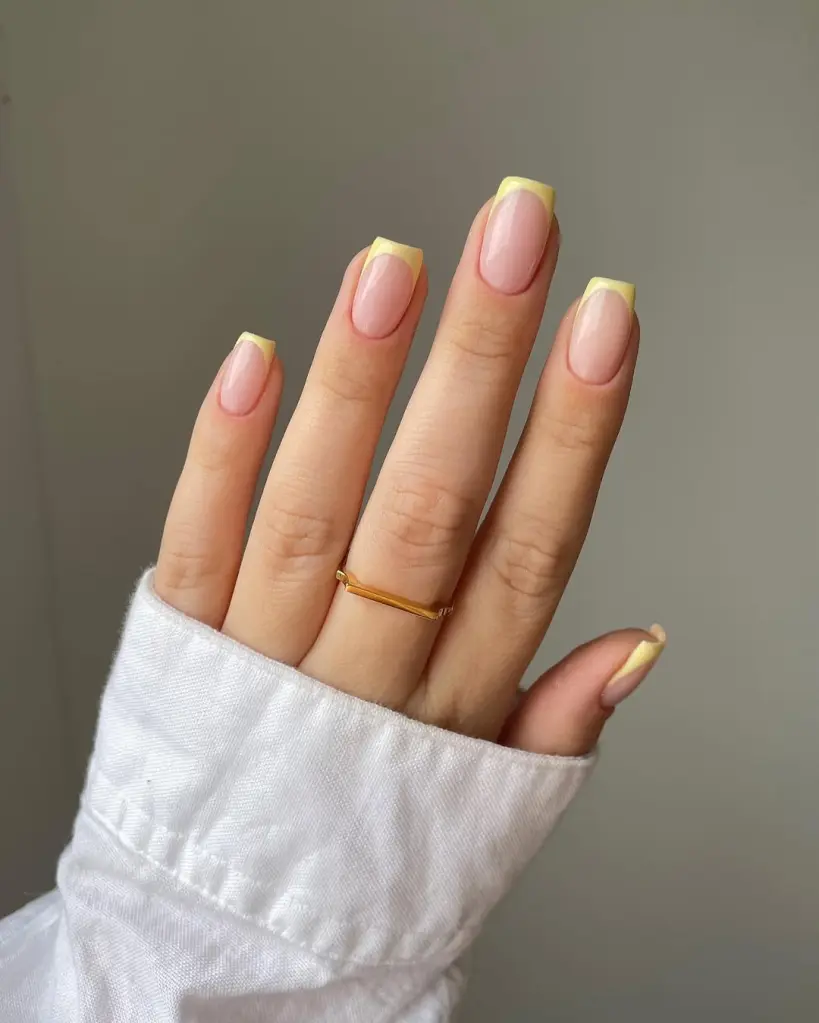 Spring Nail Ideas with squared-off yellow pastel French tips on a glossy nude background, simple and chic.
