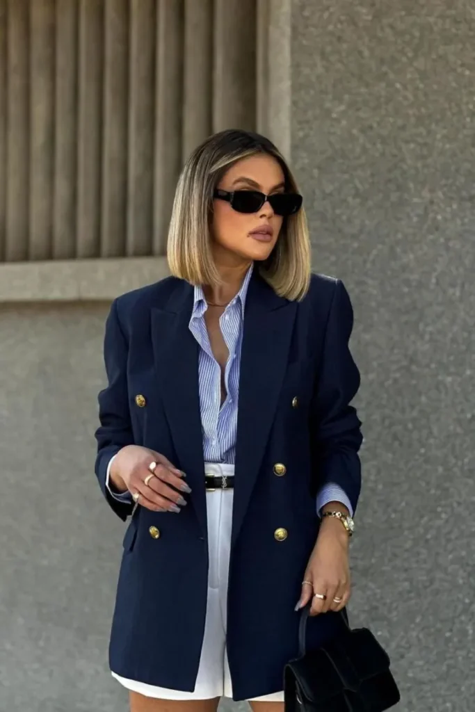 Woman in navy double-breasted blazer with gold buttons, striped shirt, and white shorts for a polished, look expensive outfit.