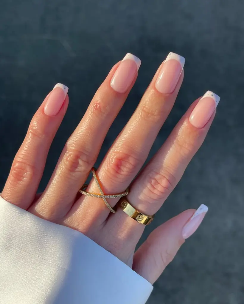 Spring Nail Ideas with classic French tips in soft white over a pink base, embellished with subtle speckled glitter.