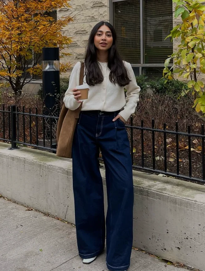 Coffee date look with a cozy white cardigan, wide-leg denim pants, and stylish sneakers, carrying a tan tote bag.