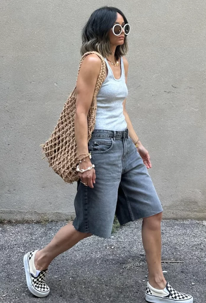 Woman in gray denim Bermuda shorts and a gray tank top with a woven net tote, styled for summer but not typically modest.
