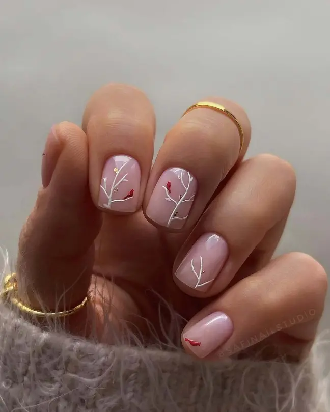 Artistic nude nail ideas with delicate white branches and red bird illustrations for a winter theme.