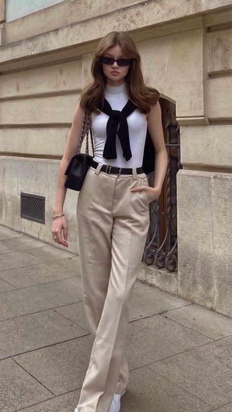 Elegant woman wearing a sleeveless white top, beige trousers, and a black sweater draped over shoulders, embodying a look expensive outfit.