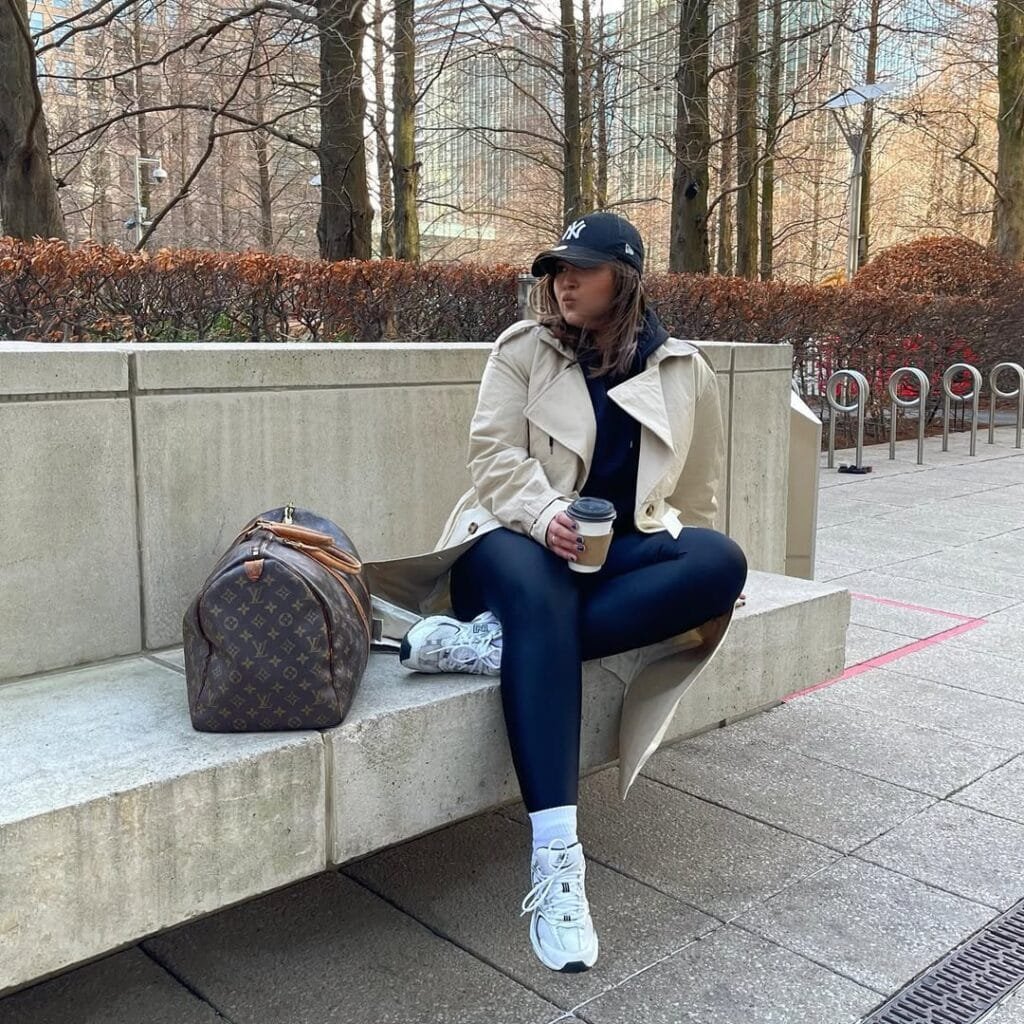 Casual coffee date look with a beige trench coat, leggings, a cap, and sneakers, complete with a Louis Vuitton bag.