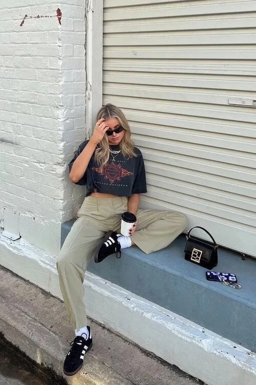Effortlessly cool look with Adidas Samba Outfits, beige trousers, graphic tee, and small structured black handbag.