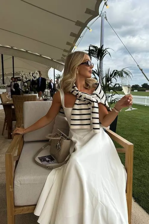 Sophisticated Summer Vacation Outfit with a white flowy dress and striped sweater draped over the shoulders, perfect for a summer event or garden party.