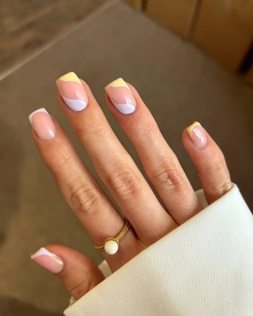 Spring Nail Ideas in swirl pastel designs with yellow and lilac curved French tips on a nude base.
