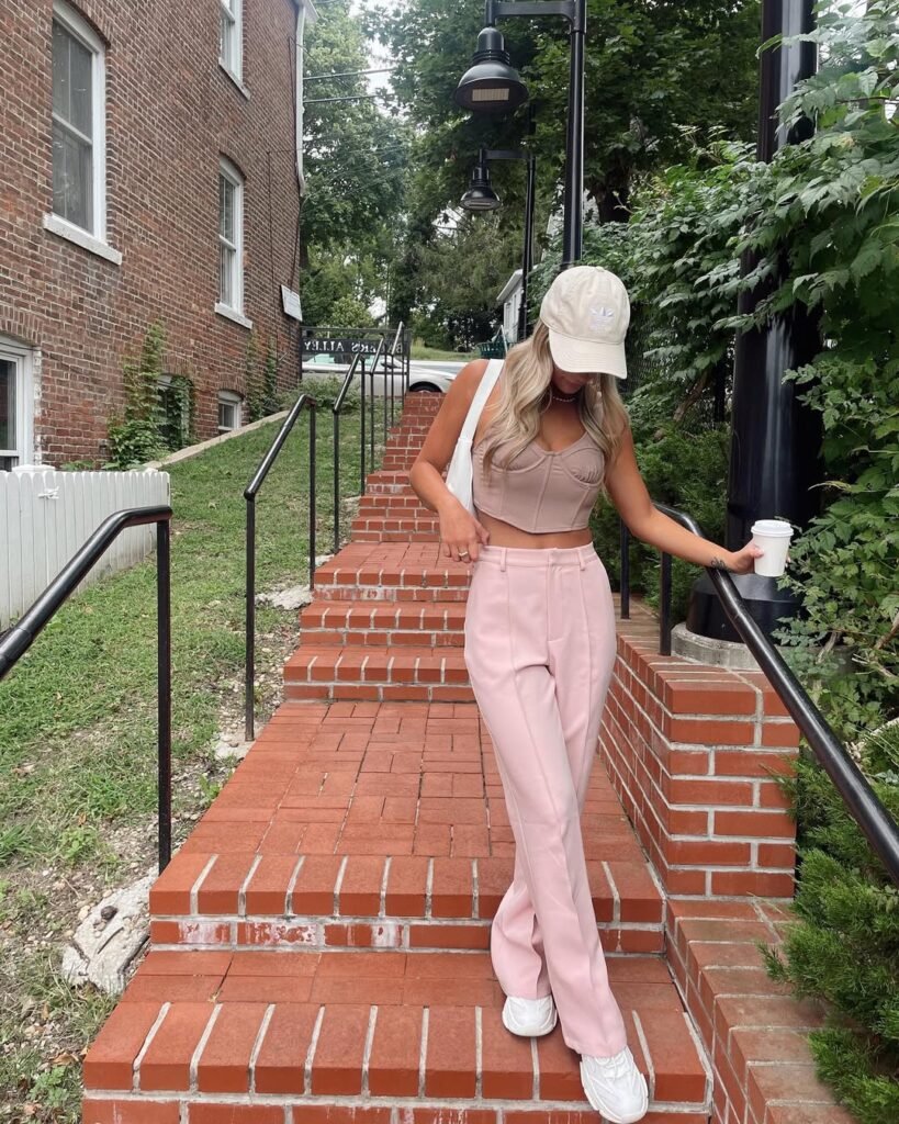 Casual yet stylish coffee date outfit featuring a beige cap, a cropped top, and pink trousers paired with white sneakers.
