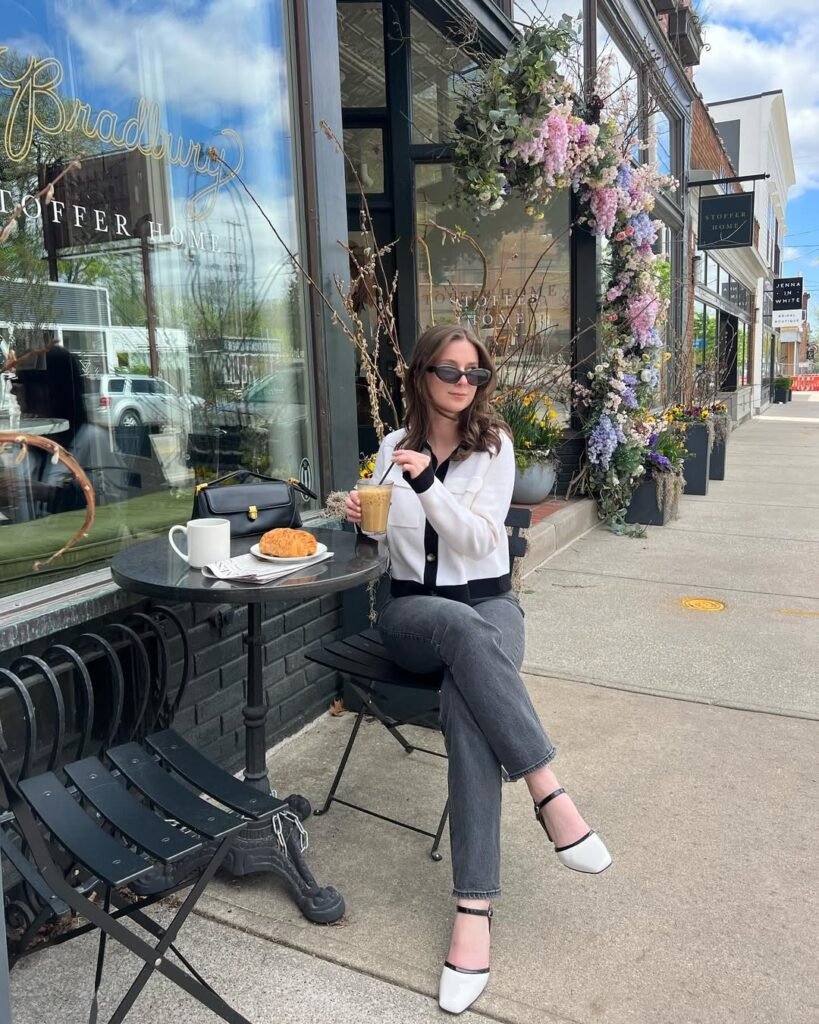 Chic coffee date outfit with a white top, gray jeans, black handbag, and stylish black-and-white heeled shoes.