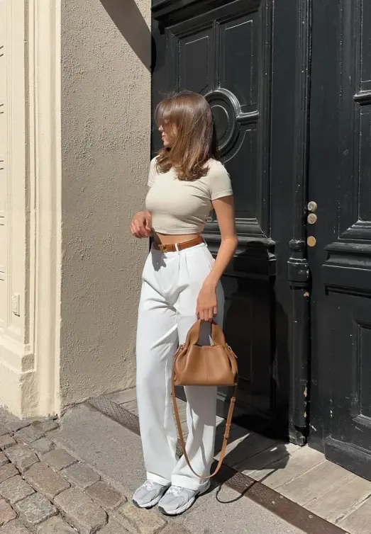 Modern Casual Summer Outfits featuring a fitted beige crop top with white high-waisted trousers, accessorized with sneakers and a tan handbag.
