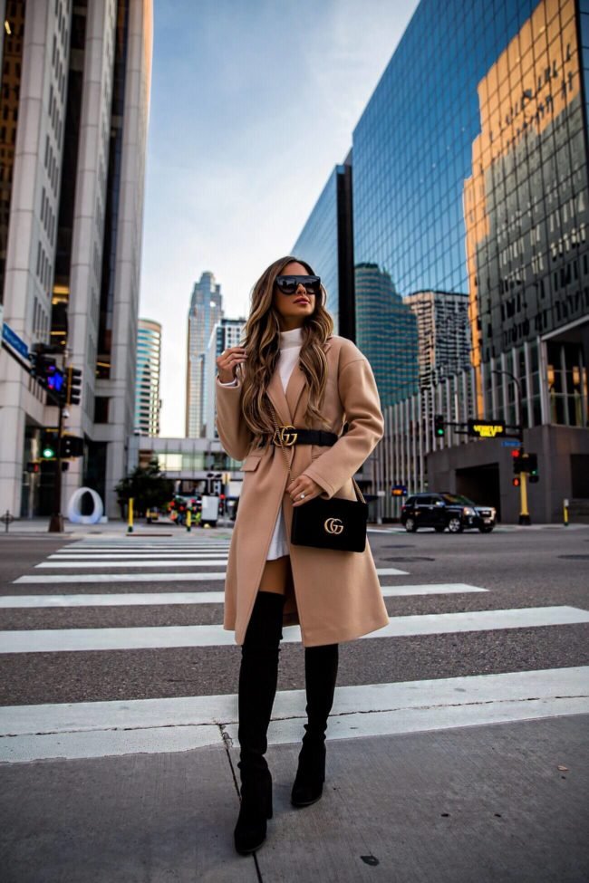 City chic look with a camel coat over a white mini dress, cinched at the waist with a designer belt and matched with thigh-high black boots — look expensive outfits.