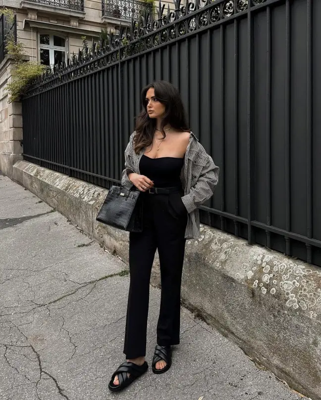 Edgy and minimalist Casual Summer Outfits with a black tube top and black trousers, topped with a striped overshirt and black accessories.