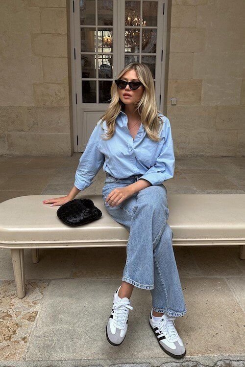 Effortlessly cool Adidas Samba Outfits with a light blue button-down shirt tucked into high-waisted light-wash jeans, styled with black sunglasses and white Samba sneakers.
