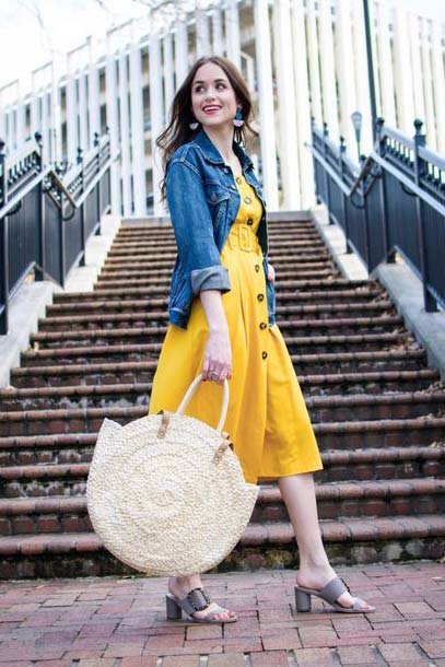 Woman in a bright yellow button-down midi dress with a denim jacket and large straw bag—playful and modest summer outfit for daytime outings.