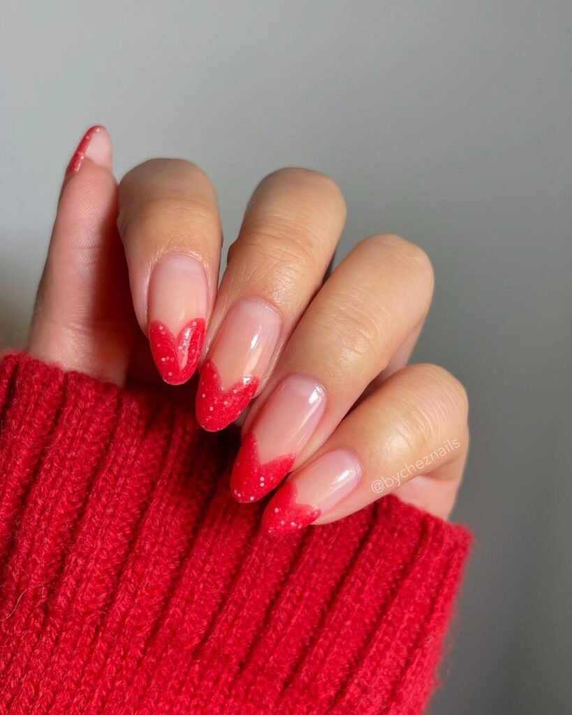 Sparkly red heart-shaped French tip nail ideas on nude almond nails for a playful and festive vibe.