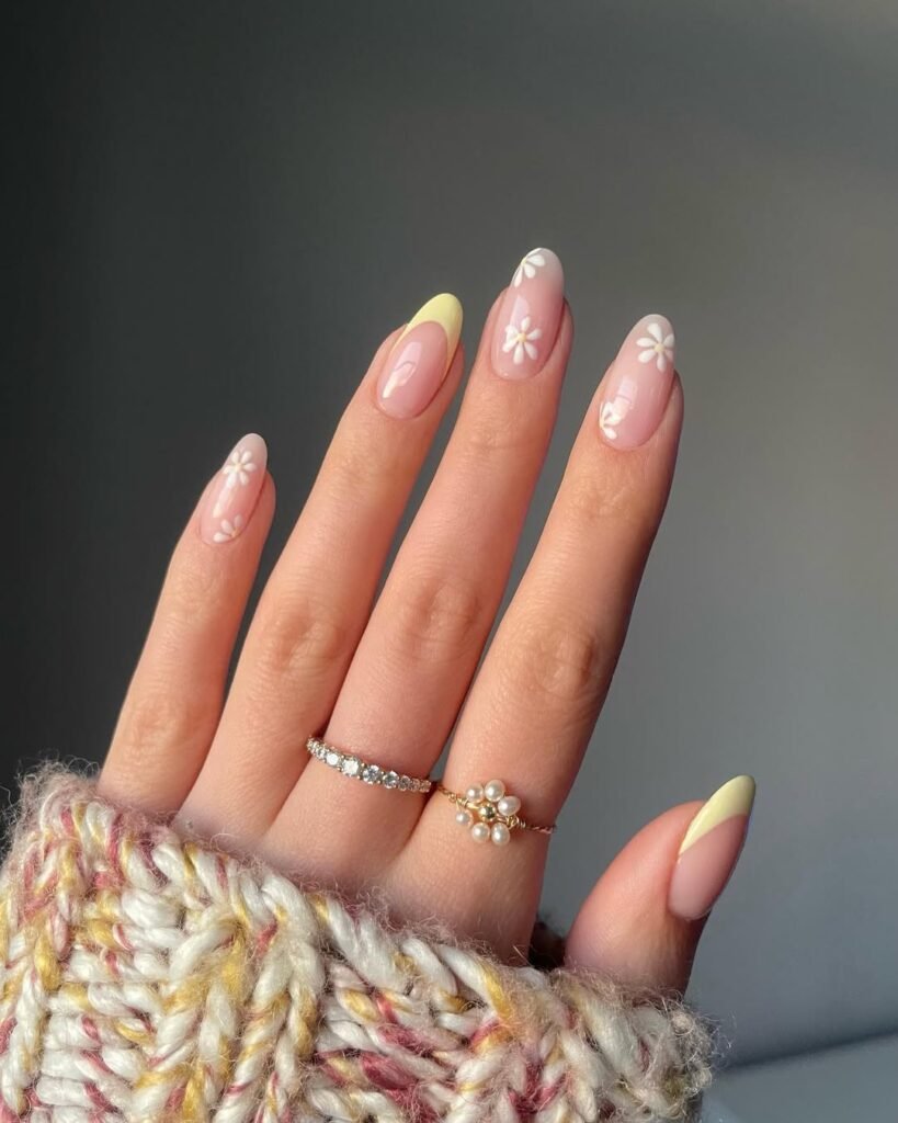 Spring Nail Ideas in soft yellow and pink French tips with white daisy flower designs on nude nails.