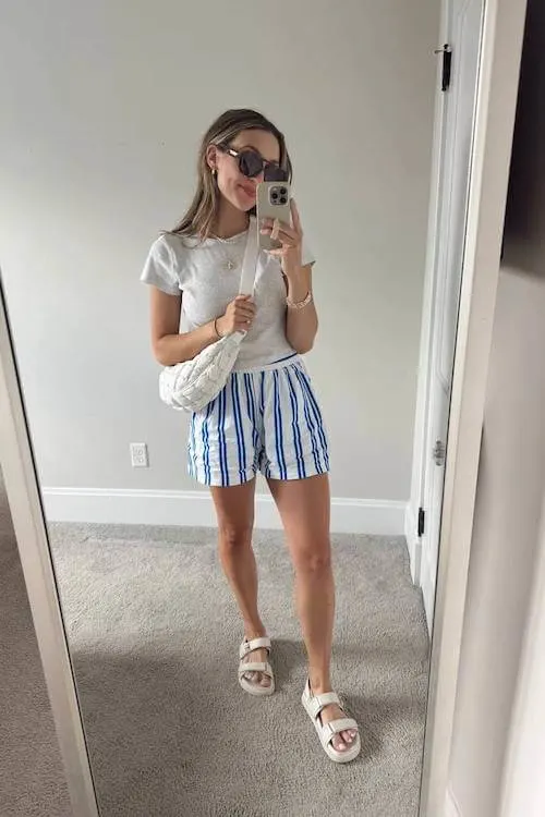 Comfy and simple Summer Vacation Outfit with a white tee, blue striped shorts, and chunky white sandals.
