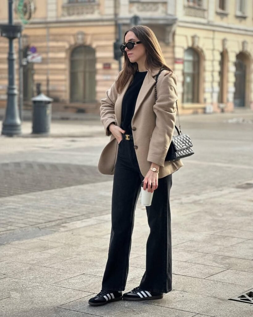 Polished neutral Adidas Samba Outfits with a tan coat over an all-black outfit, paired with black Adidas Samba sneakers and a quilted handbag for a sophisticated city look.