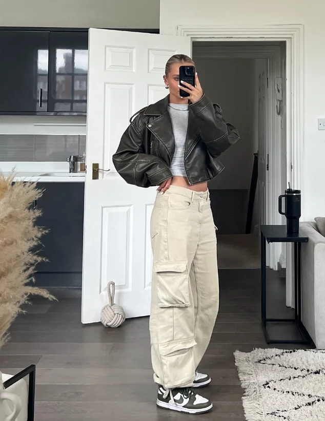 Woman in beige cargo pants, cropped gray tee, and oversized leather jacket—sporty and casual take on modest summer outfits with streetwear vibes.