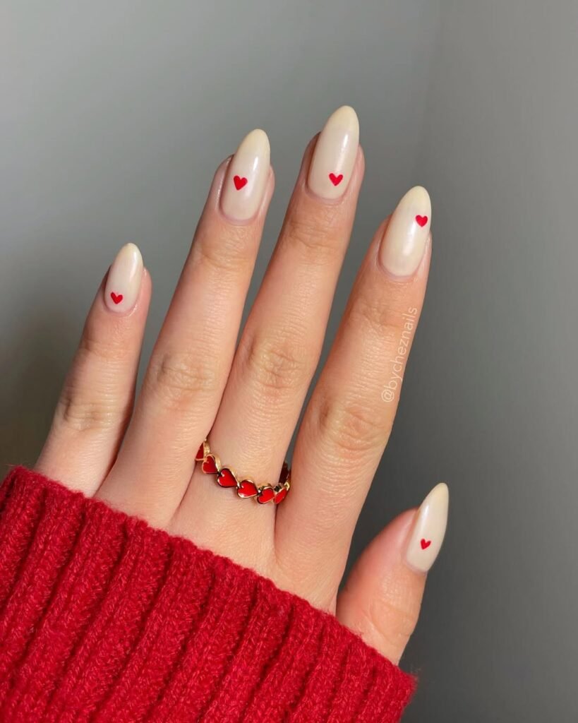 Simple and cute nail ideas with small red heart details on creamy nude almond nails.