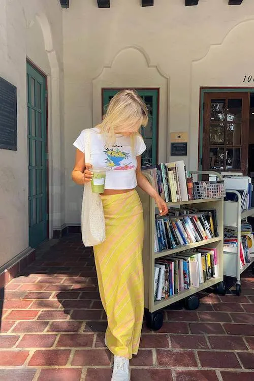 Trendy and fun Summer Vacation Outfit with a cropped graphic tee, yellow plaid maxi skirt, and white sneakers.