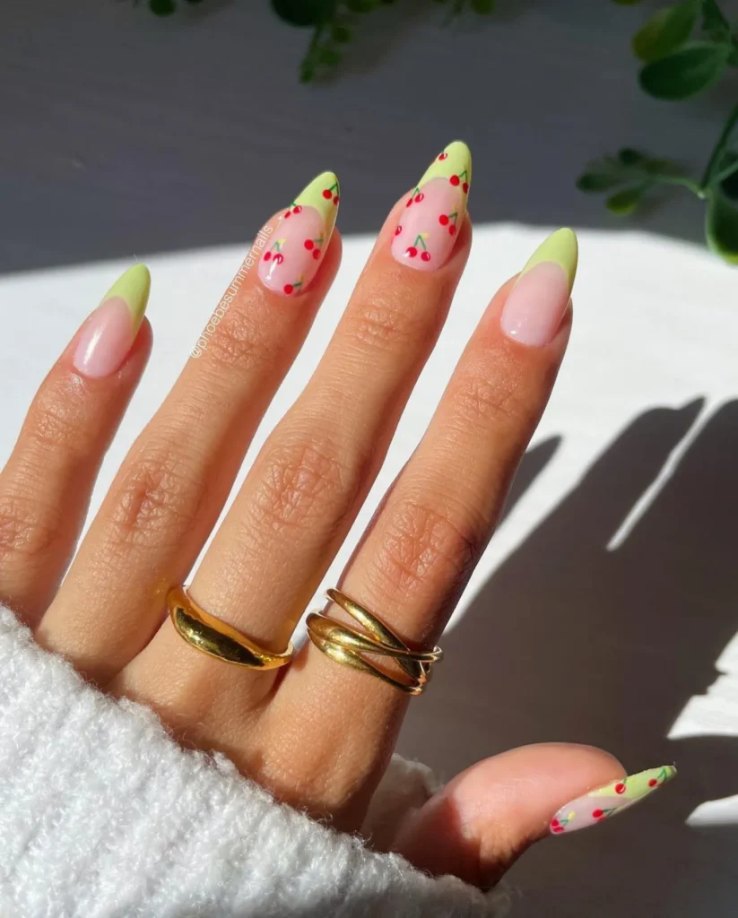 Almond-shaped nails with pastel green French tips and delicate cherry nail art on a nude base.