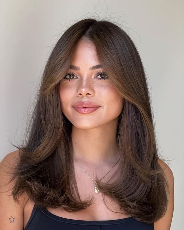 Hairstyles for Medium Length Hair featuring voluminous curtain bangs and sleek, layered ends for a polished and face-framing effect.