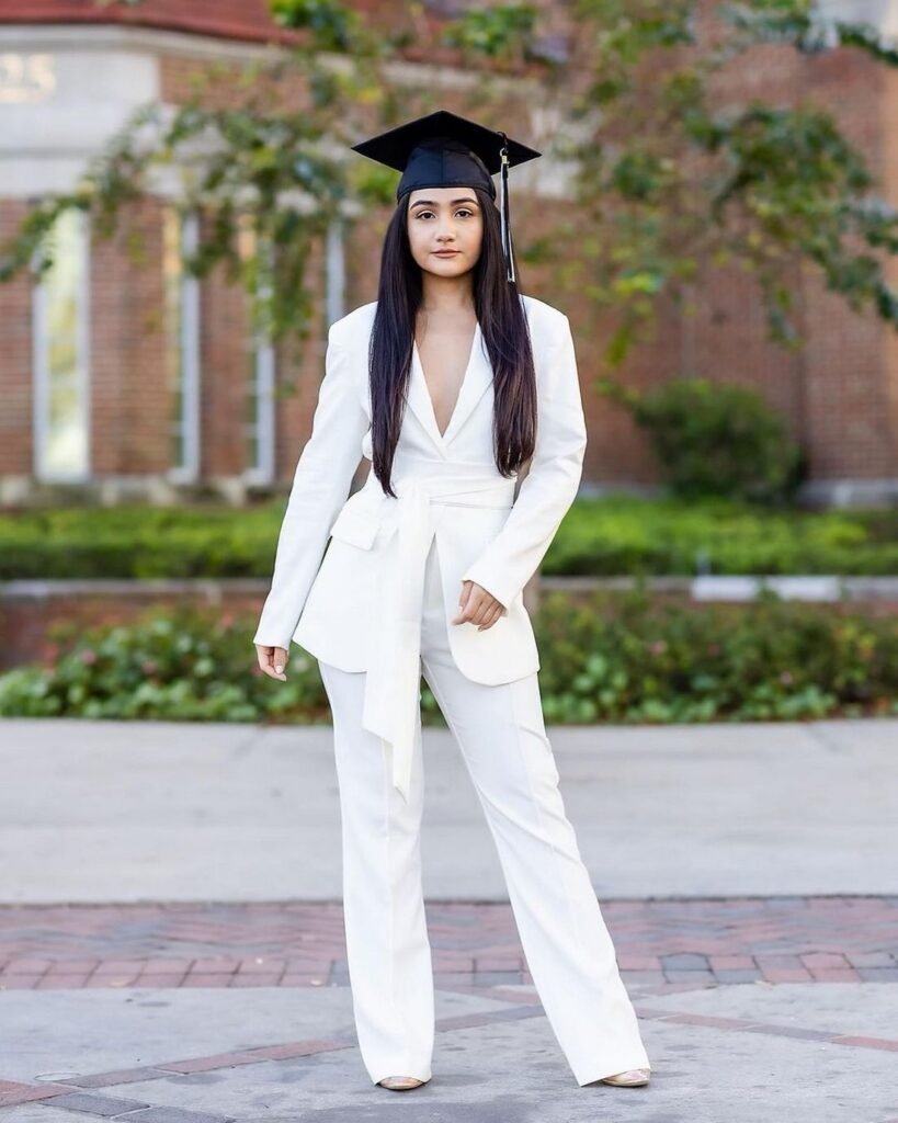 Graduation outfit ideas – tailored white pantsuit with a plunging neckline, styled with a graduation cap and minimal accessories for a sleek, fashion-forward statement.