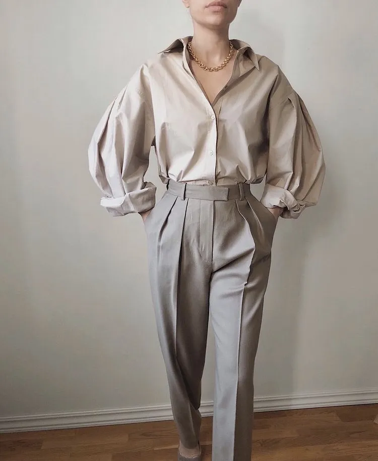 Sophisticated grey trouser outfit with a beige puff-sleeve button-down shirt, gold chain necklace, and tailored high-waisted trousers.