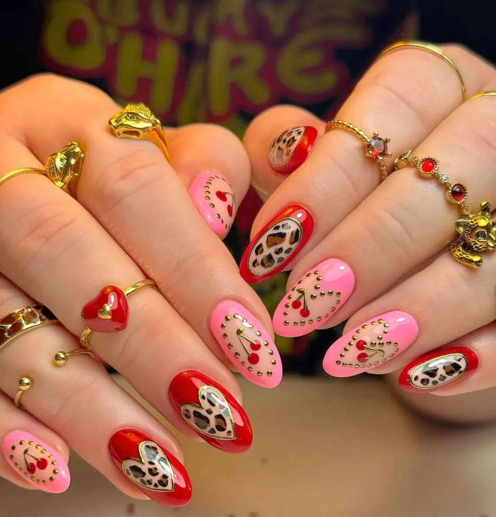 Pink and red almond nails with leopard print hearts and gold studs, featuring cherry nail art accents.