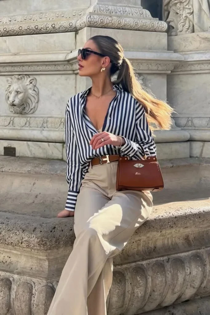 Old Money-Inspired Spring Outfit featuring a navy striped blouse tucked into beige tailored trousers, styled with a brown handbag and gold accessories.