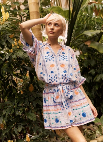 Woman wearing casual summer dress with colorful embroidered patterns, short sleeves, and a belted waist, standing in a lush garden.