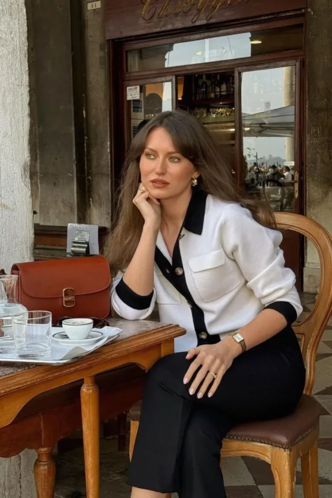 Old Money-Inspired Spring Outfit with a contrast-trim cardigan, black trousers, and a structured brown leather bag, styled for a café setting.