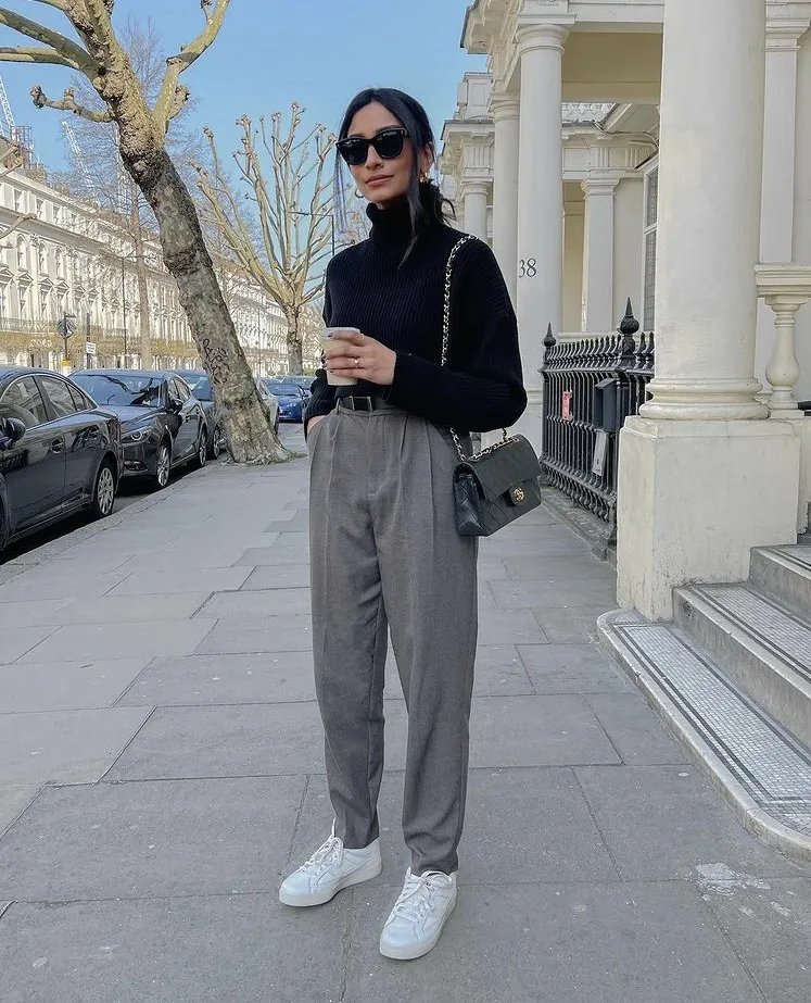 Chic grey trouser outfit paired with a black turtleneck sweater, black Chanel quilted bag, and white sneakers, worn on a city street.