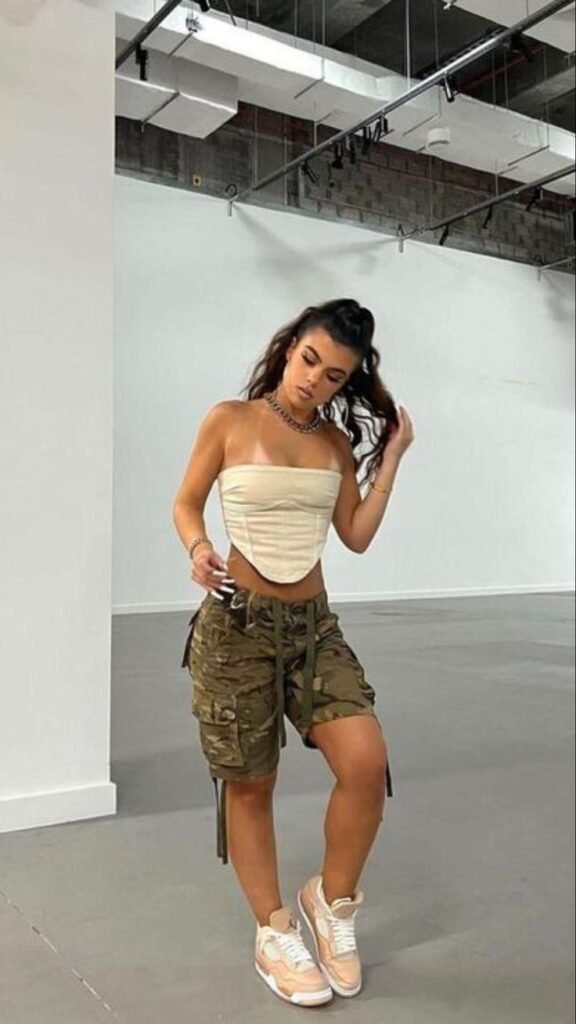 Cargo Shorts Outfits: Glam streetwear with camo cargo shorts, structured beige corset top, and sneakers.