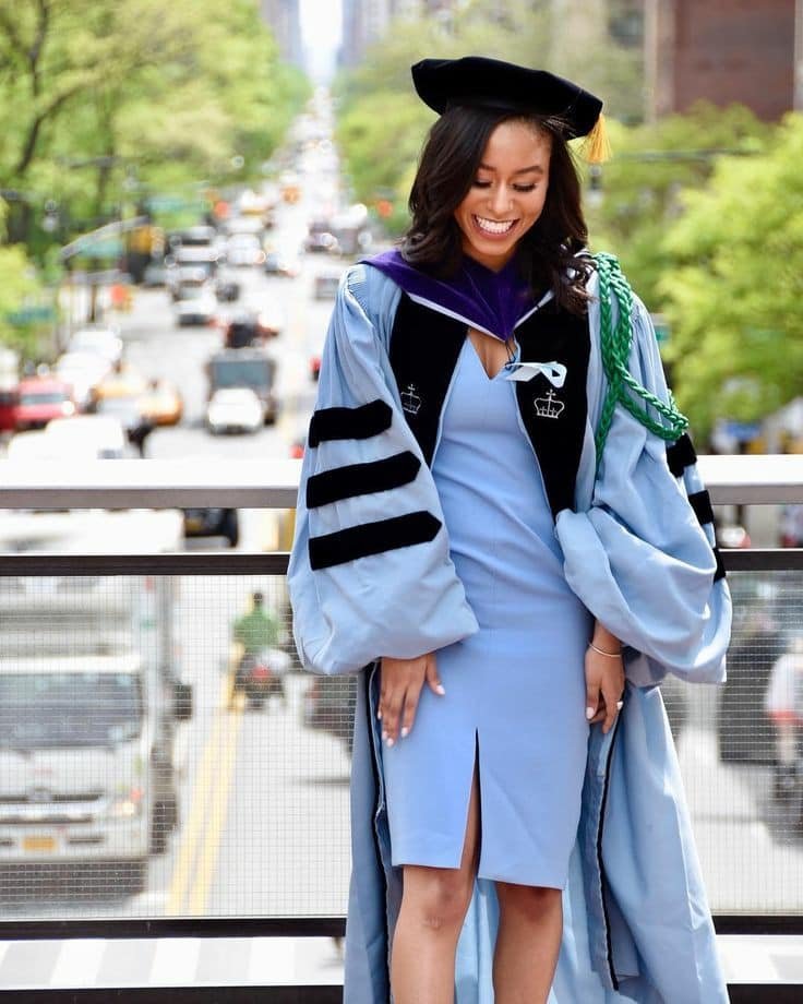 graduation outfit ideas: Light blue dress with a front slit under a formal academic gown in shades of blue and black, paired with a traditional academic cap.