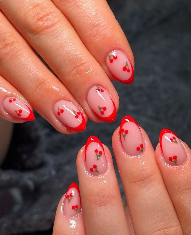 Short almond nude nails with bright red French tips and scattered cherry nail art.