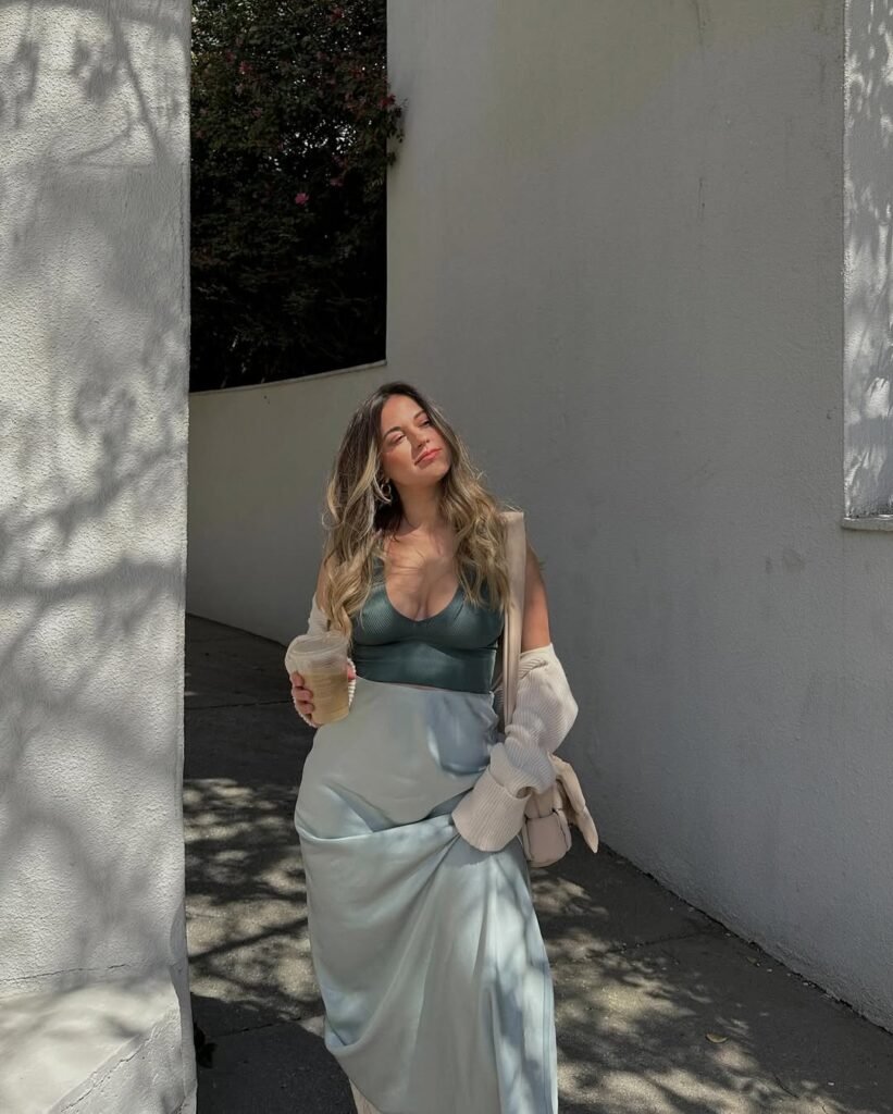 Spring Outfit Ideas featuring a silky pale blue skirt, dark green bralette, and soft knit cardigan, styled with wavy hair and iced coffee.