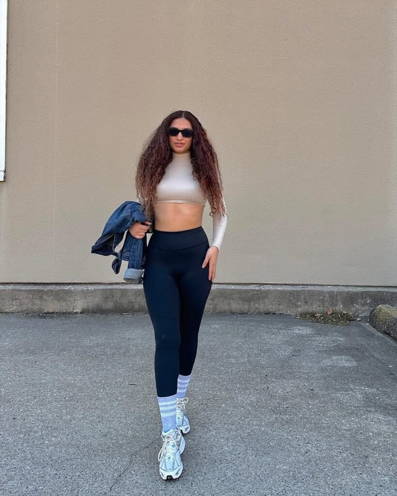 A cute simple outfit made for athleisure lovers – beige crop top, black high-waisted leggings, white sneakers, and sporty socks for a sleek streetwear look.