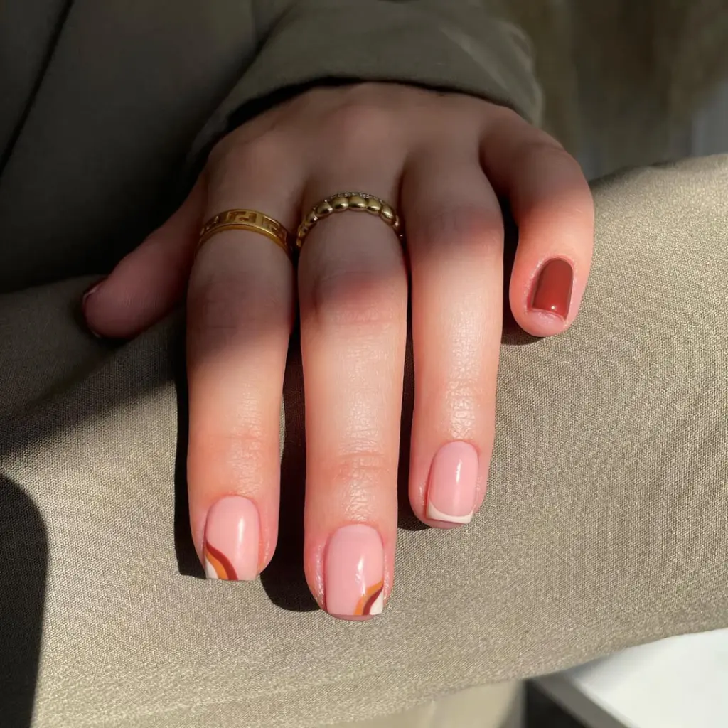 Short fall nail designs with nude base, brown swirl accents, and one solid brown nail.
