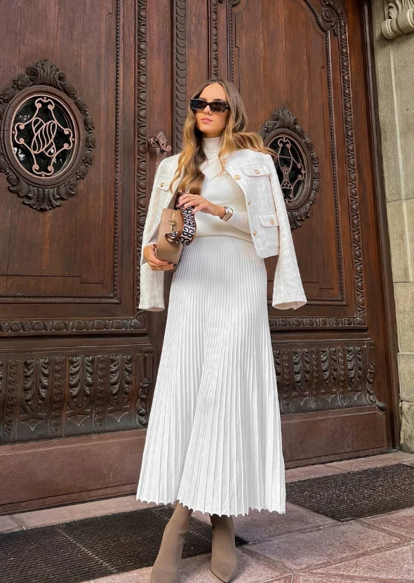 Early Fall Outfit in elegant neutrals – a pleated white midi skirt with a matching knit top and cropped jacket, styled with taupe boots for a refined city look.