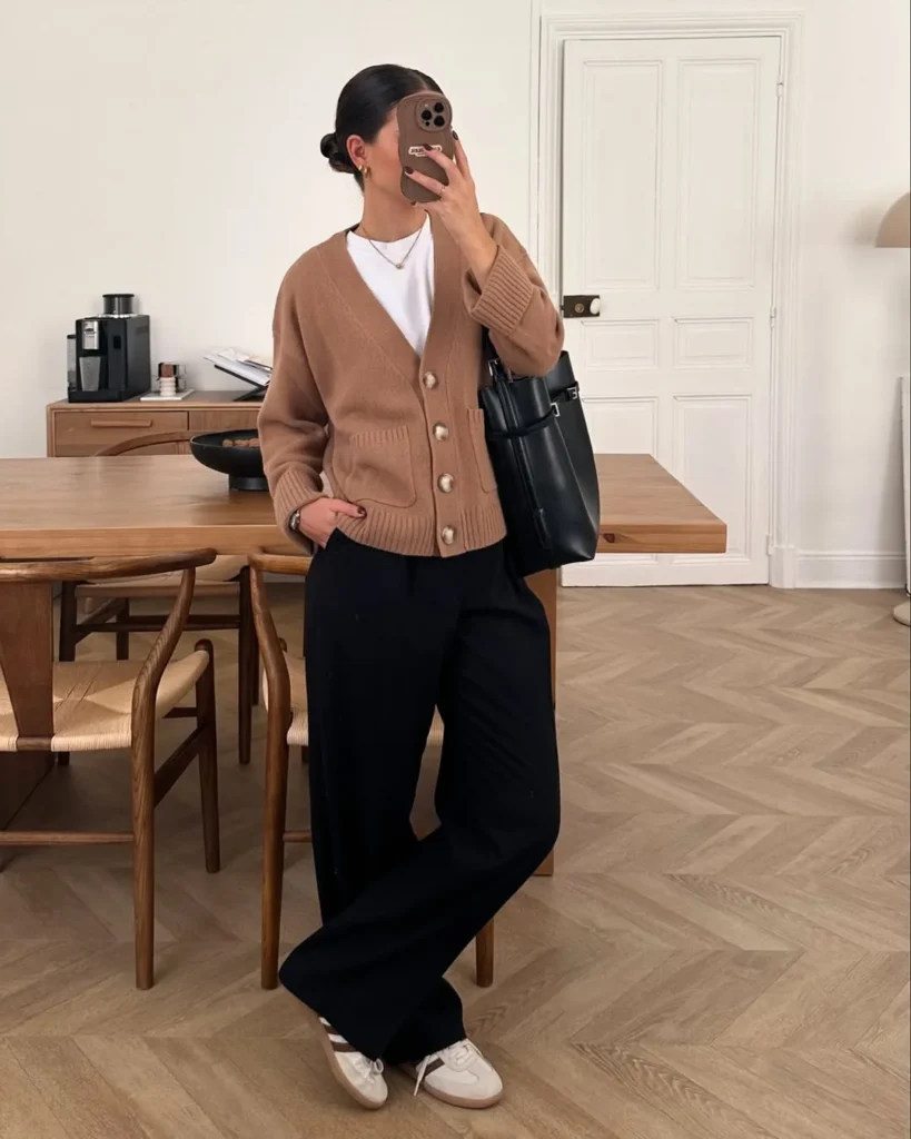 Office outfit with a camel button-up cardigan layered over a white T-shirt, paired with black wide-leg trousers, white sneakers, and a black leather tote bag.