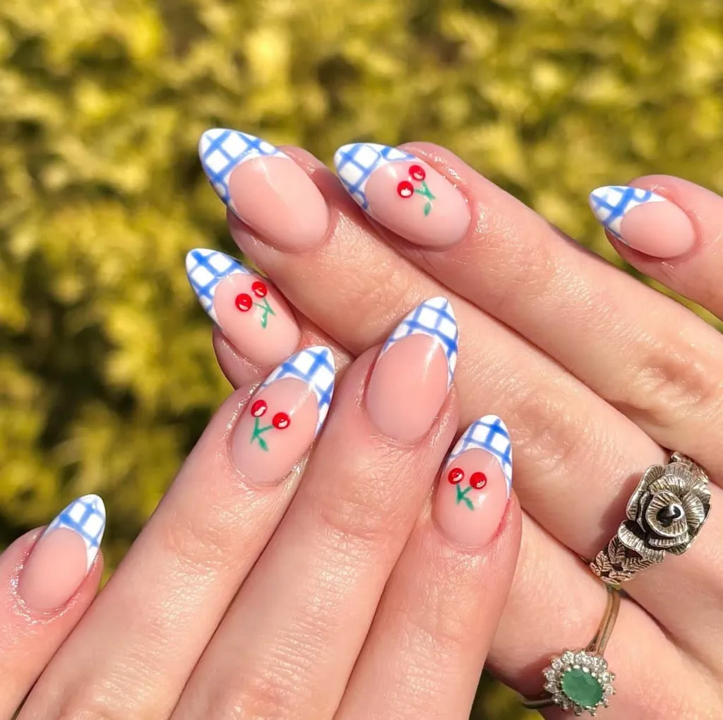 Almond nude nails with blue-and-white checkered French tips and cherry nail art accents.