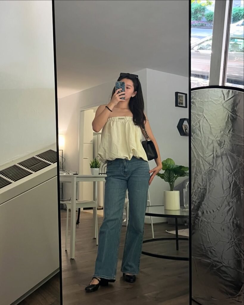 outfit korean style with a loose pale yellow strapless top paired with straight-leg blue jeans and black flats.