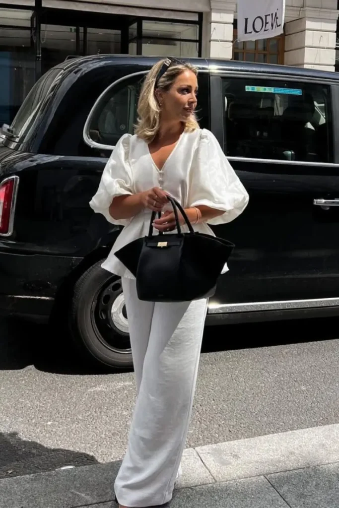 Spring Outfit Ideas showcasing a white puff-sleeve blouse and matching trousers, accessorized with a black handbag and a chic hair clip.