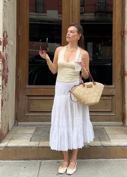 European Summer Outfit styled with a halter beige top, flowing white maxi skirt, straw tote bag, and cream flats.