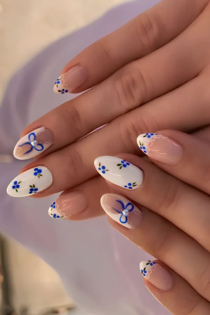White Summer Nails adorned with hand-painted blue floral designs and a pearl accent, creating a playful summer vibe.